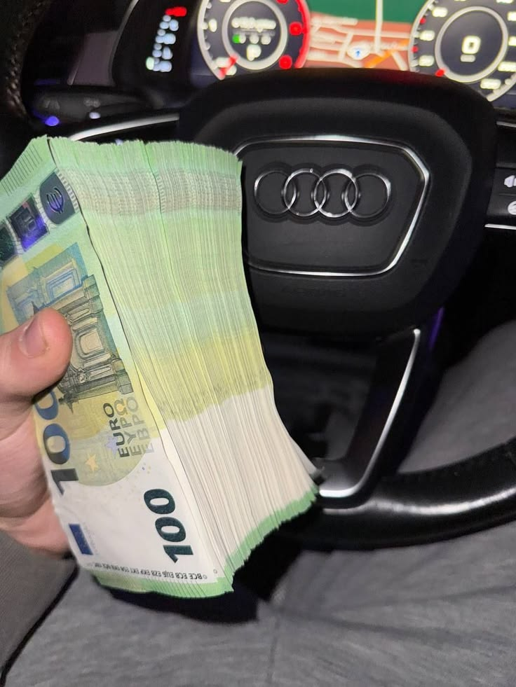 Stack of €100 notes held over a steering wheel